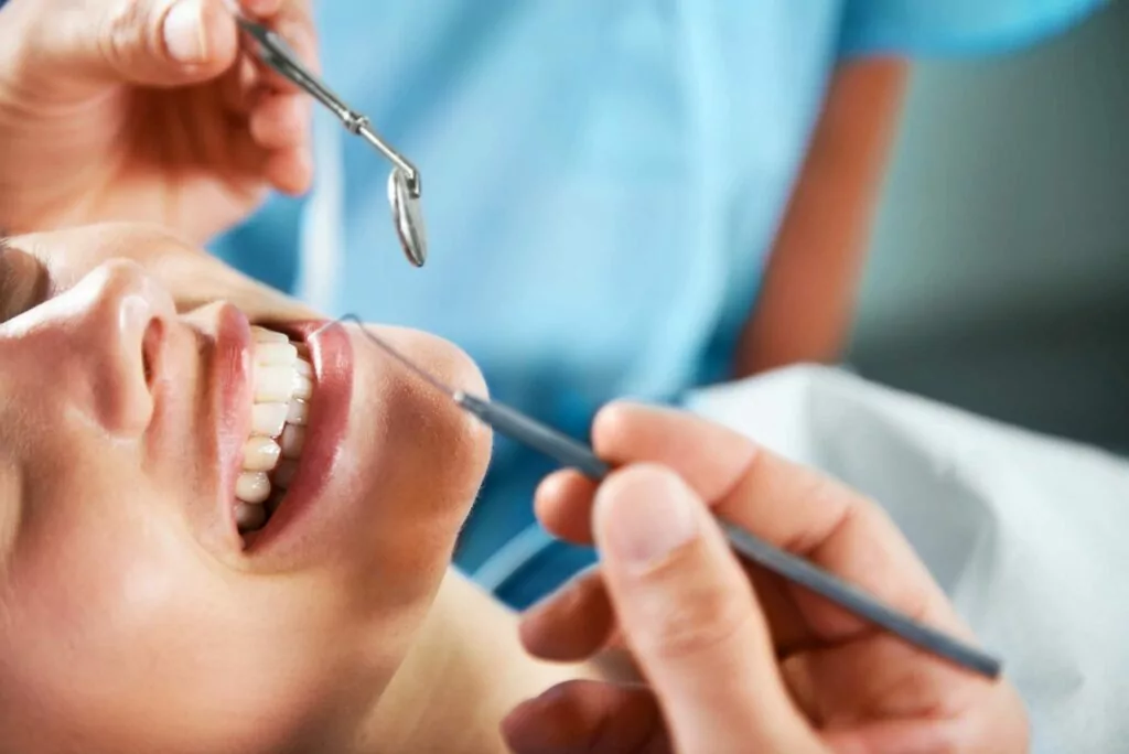 A close-up of a dental examination with a patient lying back and a dentist or dental hygienist using dental tools to inspect the patient's teeth.