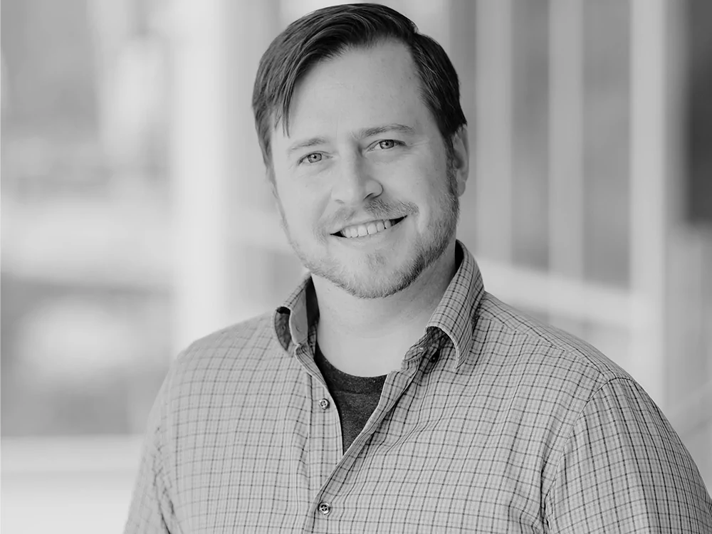 Headshot of Dr. Freihaut in a checkered shirt, indoors in a setting with glass panels or windows visible in the background. The image is in black and white.